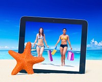 Tablet PC taking photo of women with shopping bags on a tropical beach.