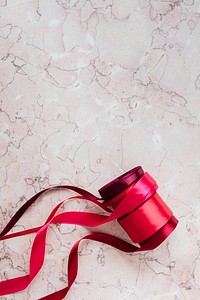 Rolls of red ribbon on a pink marble background