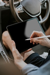 Hand holding stylus pen on a tablet screen in a car