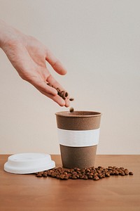 Hand pouring coffee beans into a cork coffee cup