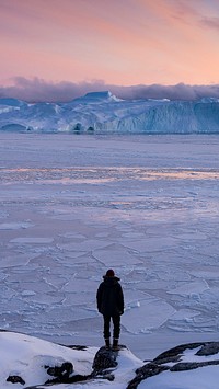 Man watching the sun setting over the frozen sea in Greenland