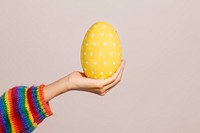 Hand holding a white polka dot patterned yellow egg on a brown background