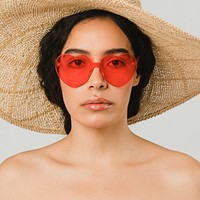 Bare chested woman wearing a big round hat and red vintage heart-shaped sunglasses