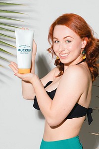 Sexy woman in a bikini holding a sunscreen tube mockup