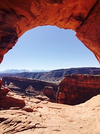 A view on a sunlit canyon from below a red rocky arch. Original public domain image from Wikimedia Commons