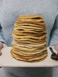 Person holding a cutting board with a stack of homemade pancakes. Original public domain image from Wikimedia Commons
