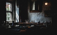 A table with plates and wine glasses in a corner of a dark restaurant room. Original public domain image from Wikimedia Commons