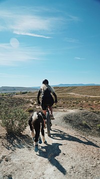 A blonde woman riding a bicycle through the desert with a dog following him in St. George. Original public domain image from <a href="https://commons.wikimedia.org/wiki/File:St._George_dog_and_bicycle_(Unsplash).jpg" target="_blank" rel="noopener noreferrer nofollow">Wikimedia Commons</a>