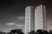 Black and white photo of a high rise apartment building with many small windows and trees. Original public domain image from Wikimedia Commons