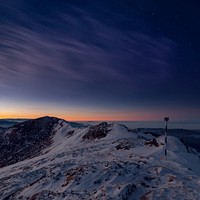 A distant sunset in the horizon as night falls over a snow covered Ciucas Peak. Original public domain image from Wikimedia Commons