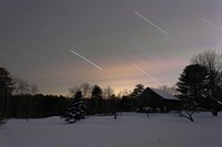 A blurred photo of light trails, with a background of silhouette building and treeline. Original public domain image from <a href="https://commons.wikimedia.org/wiki/File:Arrowsic_country_home_in_Winter_(Unsplash).jpg" target="_blank" rel="noopener noreferrer nofollow">Wikimedia Commons</a>