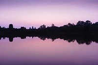 Lake shoreline is reflected in still water during a purple sunset at dusk.. Original public domain image from Wikimedia Commons