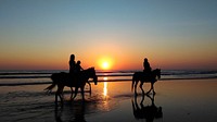 Silhouettes of people riding horses through shallow water on a beach during sunset. Original public domain image from <a href="https://commons.wikimedia.org/wiki/File:Horse_ride_on_the_beach_at_dusk_(Unsplash).jpg" target="_blank" rel="noopener noreferrer nofollow">Wikimedia Commons</a>
