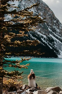 A woman in a knit cap sitting on rocks on the shore of Lake Louise. Original public domain image from Wikimedia Commons
