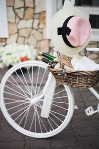 A basket with two bottles of wine and fresh bread hanging from the handlebar of a white bicycle. Original public domain image from <a href="https://commons.wikimedia.org/wiki/File:Wine_and_bread_(Unsplash).jpg" target="_blank" rel="noopener noreferrer nofollow">Wikimedia Commons</a>