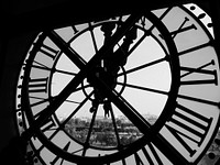 A black and white shot from behind a clock looking out into Paris. Original public domain image from <a href="https://commons.wikimedia.org/wiki/File:Behind_a_clock_(Unsplash).jpg" target="_blank" rel="noopener noreferrer nofollow">Wikimedia Commons</a>