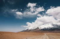 Road in the plains leading to cloud-covered snowy mountains in Licancabur. Original public domain image from Wikimedia Commons