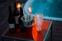 A tabletop containing wine, straws, candles with flames and plastic cups by a pool in redding. Original public domain image from Wikimedia Commons