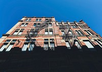 A brick residential building with fire escapes against a blue sky in Montreal. Original public domain image from <a href="https://commons.wikimedia.org/wiki/File:Montreal_apartments_(Unsplash).jpg" target="_blank" rel="noopener noreferrer nofollow">Wikimedia Commons</a>