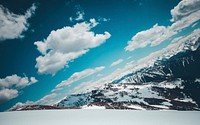 An angular shot of snow-capped mountains under fluffy clouds. Original public domain image from <a href="https://commons.wikimedia.org/wiki/File:Schwalbenwand_(Unsplash).jpg" target="_blank" rel="noopener noreferrer nofollow">Wikimedia Commons</a>