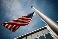 Looking up at a flagpole with the American flag flying half mast. Original public domain image from <a href="https://commons.wikimedia.org/wiki/File:Flying_Half_Mast_(Unsplash).jpg" target="_blank" rel="noopener noreferrer nofollow">Wikimedia Commons</a>