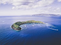 A crescent moon shaped island in the middle of a bright blue ocean at Molokini Crater. Original public domain image from Wikimedia Commons