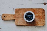 White cup of blueberries on top of cutting board on top of wooden surface. Original public domain image from <a href="https://commons.wikimedia.org/wiki/File:NotRedBerries_(Unsplash).jpg" target="_blank" rel="noopener noreferrer nofollow">Wikimedia Commons</a>