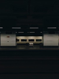 A dim shot of a metal bench on the other side of a railway platform. Original public domain image from Wikimedia Commons