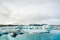 Small icebergs in bright turquoise blue water with thick clouds above. Original public domain image from <a href="https://commons.wikimedia.org/wiki/File:Vatnaj%C3%B6kull_Glacier,_Iceland_(Unsplash).jpg" target="_blank" rel="noopener noreferrer nofollow">Wikimedia Commons</a>