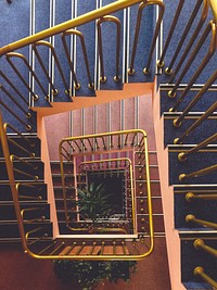 Looking down at a vintage spiral staircase with a gold banister. Original public domain image from Wikimedia Commons