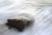 A lone weathered rock enveloped by the frothy sea waves. Original public domain image from Wikimedia Commons
