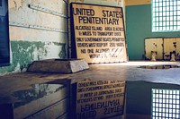 Puddle in an abandoned jail cell reflects old yellow sign for the United States Penitentiary.. Original public domain image from Wikimedia Commons