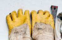 A pair of dirty yellow rubber gloves for gardening or carpentry besides a tool. Original public domain image from Wikimedia Commons