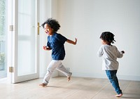 Two black kids playing and chasing each other in an empty room