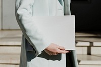 Woman in an overcoat carrying a white box in front of a building