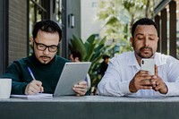 Men working with digital devices in a cafe