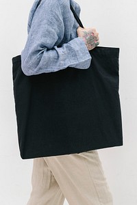 Tattooed woman in a blue linen shirt holding a black tote bag