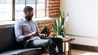 Black man using a stylus with a digital tablet on a couch social template