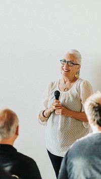 Cheerful elderly woman speaking on a microphone in a seminar