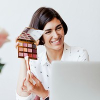 Happy women displaying an eye shadow palette with a laptop
