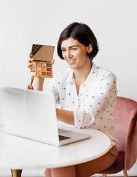 Happy women displaying an eye shadow palette with a laptop