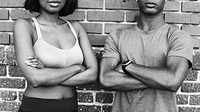 Sporty couple standing with arms crossed by a brick wall