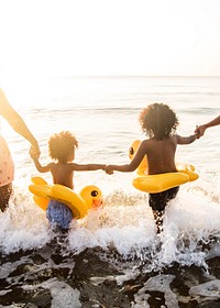 Black siblings holding hands at the beach during sunset