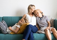 Blonde mom kissing her son&rsquo;s head and relaxing with daughter on the couch text space 