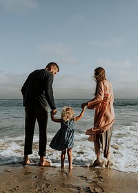 Parents holding daughter&#39;s hand at the beach text space 