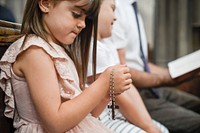 Little catholic girl praying with a rosary in her hands