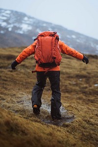 Woman in an orange windbreaker hiking under the rain at the Faroe Islands