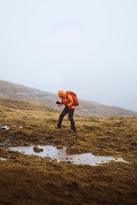 Woman in an orange windbreaker hiking under the rain at the Faroe Islands
