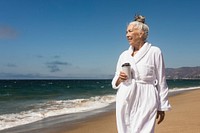 Senior woman in a bathrobe enjoy morning coffee at the beach