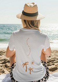 Woman in panama hat wearing white screened tee chilling at the beach back view